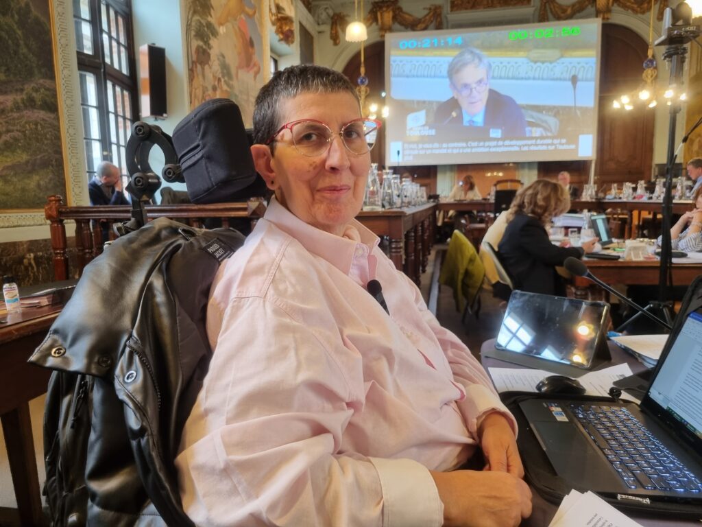 Odile Maurin de profil au 1er plan (sans masque car la pièce était ien ventilée) dans son fauteuil et en arrière plan la salle du conseil municipal et l'écran qui projete les intervenants (ici François Chollet en charge de la qualité de l'air)