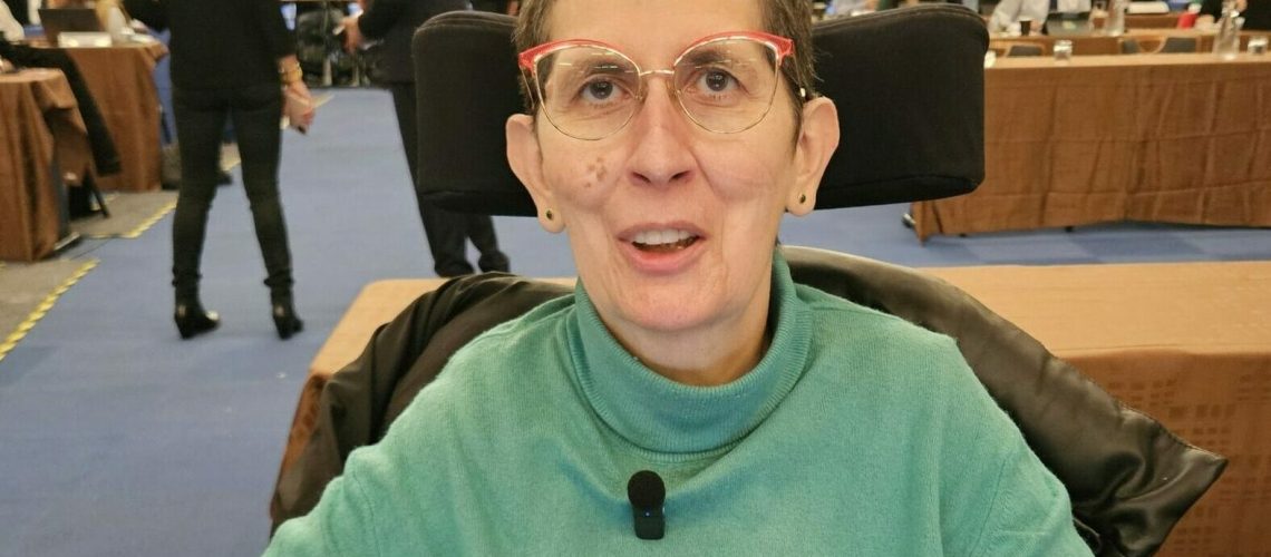 photo d'Odile Maurin dans son fauteuil roulant devant son ordinateur dans la salle du conseil métropolitain du 17 octobre 24